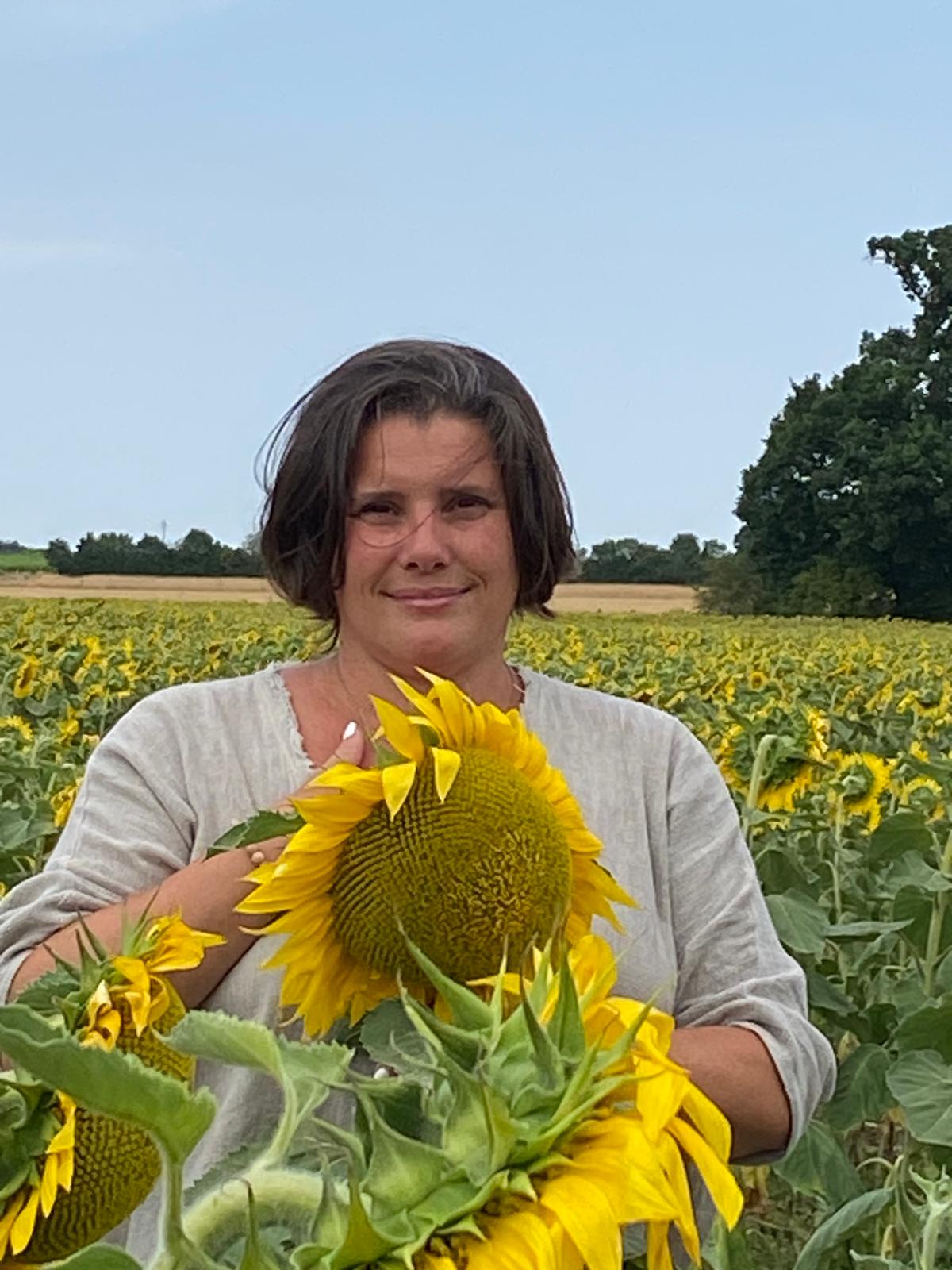 Moi dans un champ de tournesol une main en gratitude et un tournesol à la place de mon plexus solaire et mon coeur en signe de lumière